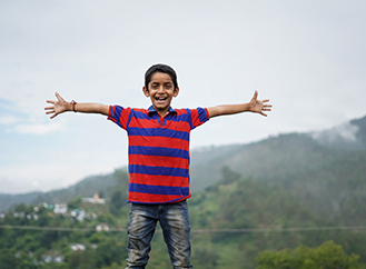Young boy with arms stretched out in front of a mountain landscape